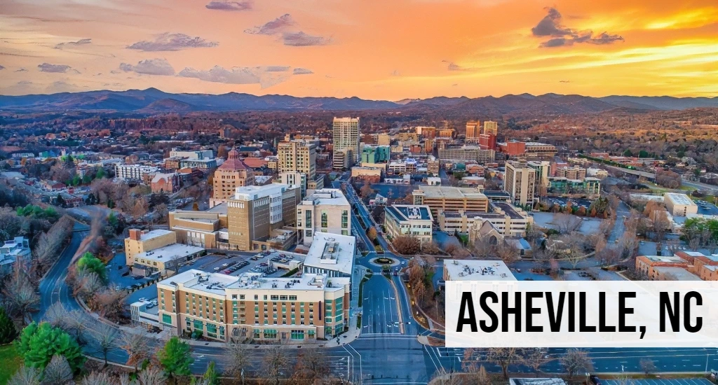 Asheville, North Carolina aerial view of downtown with city buildings, streets, and surrounding mountain landscape.